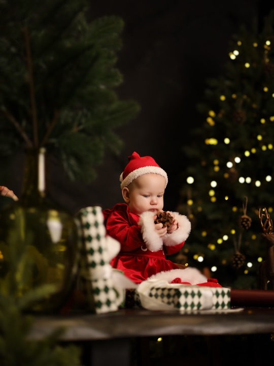 A baby in a red festive outfit holding a pine cone