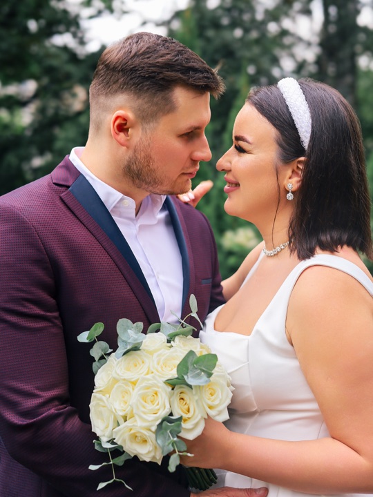 A wedding couple with a white bouquet against a leafy background