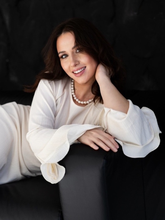 A smiling woman in white resting on a black armchair